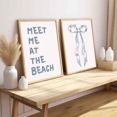 two framed art prints sitting on top of a wooden bench next to a vase with dry grass in it