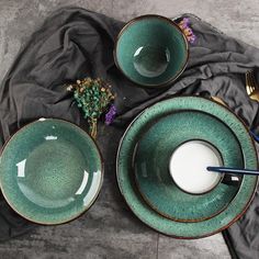 two green bowls with spoons and one bowl filled with milk on a black cloth