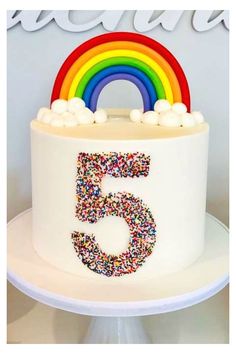 a white cake with sprinkles and a rainbow on top that says 5