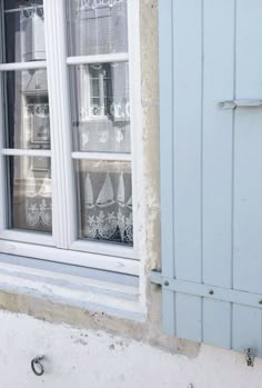 a cat sitting on the ledge of a window sill in front of a blue shutter