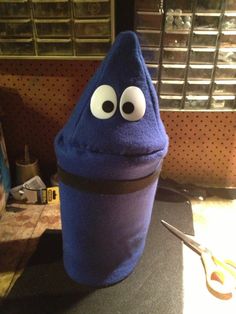 a blue hat with googly eyes sitting on top of a table next to a pair of scissors