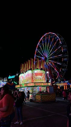 an amusement park at night with ferris wheel and carnival rides in the background as people look on