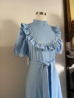 "DESCRIPTION * Vintage 70s Light Blue Sweet Maxi Dress *Bib Style with Ruffled Details and Perfect Daisy Lace Trim *Dramatic Mockneck Collar with Ruffle * Zipper from Top to Bottom * Belted around the middle  *Fit and Flare silhouette  *Short sleeves with Dramatic Cuffs *Paired perfectly for an Engagement shoot  DETAILS *Label: Handmade *Size: Small to Medium; See measurements Below *Color: Light Blue *Material: 100% Polyester *Care: Machine Wash Cold. Hang Dry. *Condition: Great quality vintage Vintage Light Blue Ruffled Dress, Vintage Light Blue Dress With Ruffles, Light Blue Vintage Dress With Ruffles, Blue Vintage Dress With Ruffles For Spring, 1970s Blue Fitted Dress, 1970s Fitted Ruffle Vintage Dress, 1970s Vintage Dress With Ruffles, Blue Vintage Style Dress For Spring, Blue Vintage Dress For Spring