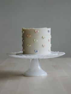 a white cake with hearts on it sitting on top of a table in front of a gray wall