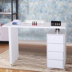 a white desk with three drawers and four bottles on the top, in front of a floral wallpapered background