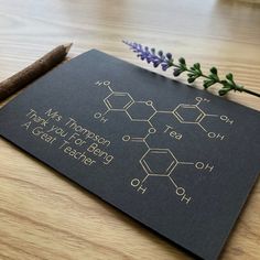 a black card with some writing on it next to a purple flower and a brown stick