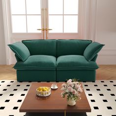 a green couch sitting in front of a window next to a table with fruit on it