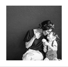 a mother and her daughter eating ice cream in front of a black wall with white trim