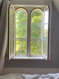 an open window in the corner of a room with white sheets and drapes on it