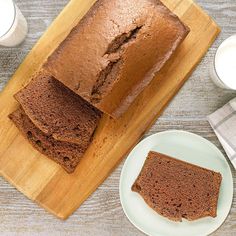 a loaf of chocolate cake sitting on top of a wooden cutting board next to a plate