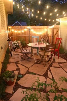 an outdoor patio with lights strung over it and chairs around the table in the middle