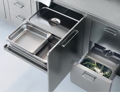 an open drawer on the side of a stainless steel kitchen counter with dishes in it