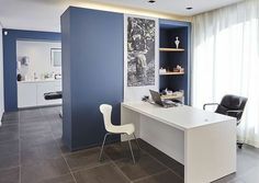 a modern office with blue walls and white furniture in the corner, along with a large window