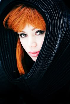 a woman with red hair and blue eyes wearing a black hoodie over her head