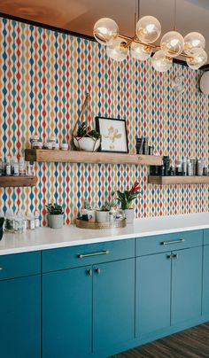 a kitchen with blue cabinets and colorful wallpaper on the walls, along with potted plants