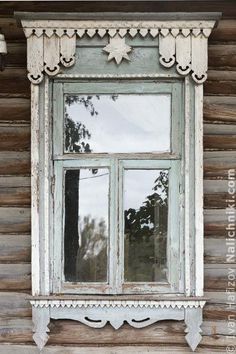 an old window with white trim on the side of a wooden building, reflecting trees and sky