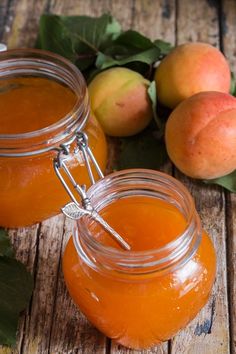 two jars filled with liquid sitting on top of a wooden table next to peaches