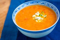 a blue and white bowl filled with soup on top of a cloth covered tablecloth