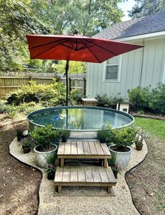 an umbrella over a small pool in a backyard with wooden benches and potted plants