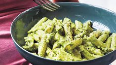 a person holding a fork in a bowl filled with green pasta and pesto sauce