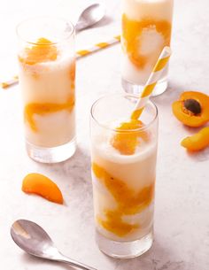 two glasses filled with ice and orange peels next to spoons on a table