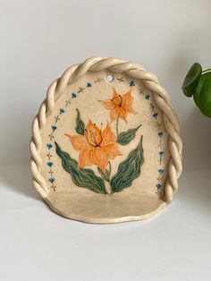 a ceramic dish with flowers painted on the side and rope around it, sitting next to a potted plant