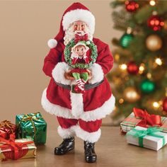 a santa clause figurine holding a christmas wreath next to presents on a table