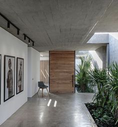 an empty room with pictures on the wall and plants in the foreground, next to a wooden door