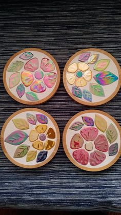 four wooden plates with painted designs on them sitting on a table top next to each other