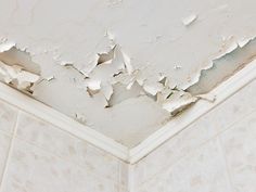 peeling paint on the ceiling of a bathroom with white walls and tile flooring that has been stripped off