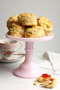 some biscuits are on a pink cake stand next to a tea cup and saucer