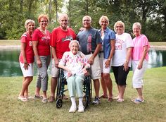 a group of older people standing next to each other in front of a lake and trees