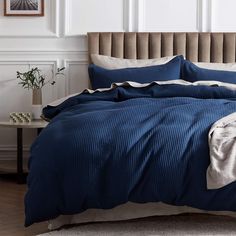 a bed with blue comforter and pillows in a white room next to a table