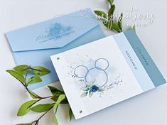 two greeting cards with blue envelopes on top of each other and some green leaves