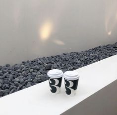 two coffee cups sitting on top of a white table next to rocks and water fountain