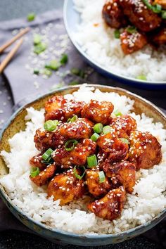 two plates filled with rice and chicken on top of each other, next to chopsticks