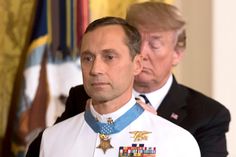 two men in suits and ties standing next to each other with flags on the wall behind them