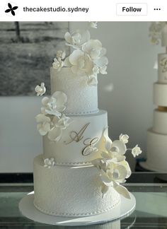 a three tiered wedding cake with white flowers on top and monogrammed lettering