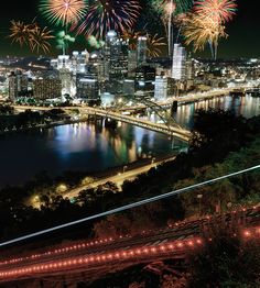 fireworks in the sky over a city at night with lights on and bridge going across