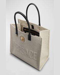 Versace canvas and acrylic tote bag with embossed logo and Medusa head accent     Rolled top handles     Open top with snap strap closure     Interior, one zip pocket    Approx. 11.4"H x 15"W x 7.4"D    "La Medusa" is made in Italy Designer Canvas Bag With Top Handle For Errands, Designer Canvas Bag With Top Carry Handle For Errands, Beige Double Handle Bag With Logo, Designer Top Handle Satchel With Logo, Designer Everyday Bags With Logo, Designer Canvas Tote Bag With Top Handle, Designer Canvas Tote Bag With Top Carry Handle, Designer Canvas Tote Bag For Errands, Designer Tote Canvas Bag For Errands