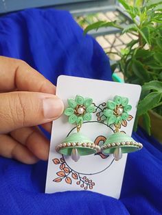 a person holding up a green pair of earrings with flowers on them and pearls in the middle