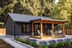 a small house with a covered patio and seating area in the middle of some flowers