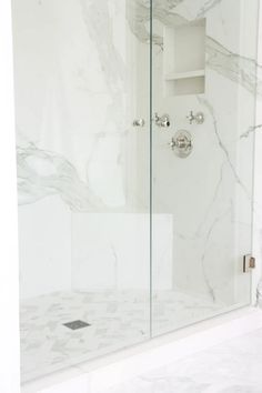 a white marble bathroom with glass shower doors and no door knobs on the side