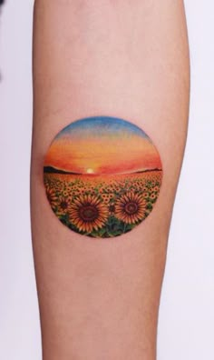 a sunflower tattoo on the left inner arm and leg, with an orange sky in the background