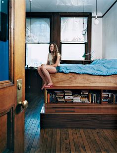 a woman sitting on top of a bed next to a book shelf filled with books