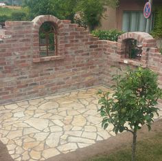 a brick wall with a small tree in the foreground and bushes on either side