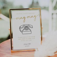 a wedding guest book with an old phone on the front and gold frame, sitting on top of a wooden table