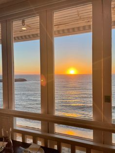 the sun is setting over the ocean from inside a restaurant with large windows that look out onto the water