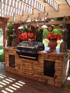 an outdoor bbq grill with potted flowers on the counter and sun shining through the roof