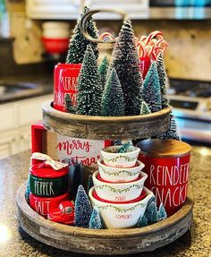 three tiered tray with christmas themed cups and trees on the top, sitting on a kitchen counter